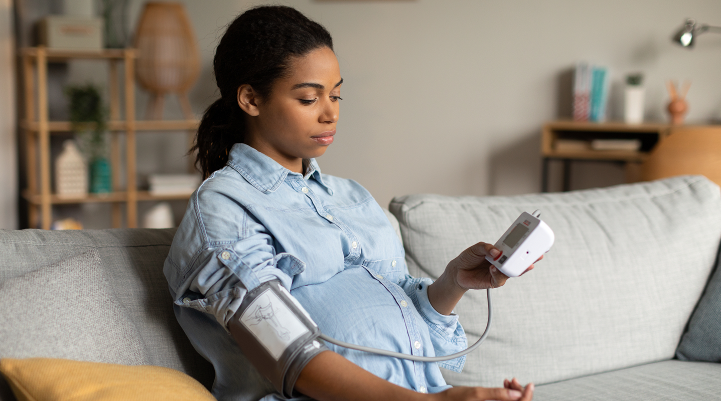 pregnant woman taking blood pressure sitting on couch