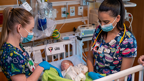 Two NICU nurses swaddling newborn