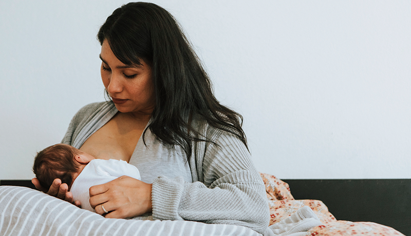 mother breastfeeding newborn on pillows